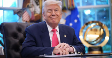A smiling Donald Trump sits with his hands folded at his Oval Office desk
