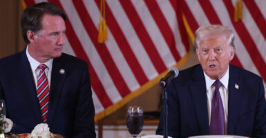 Governor Glenn Youngkin sits at a table next to Donald Trump. American flags in the background.