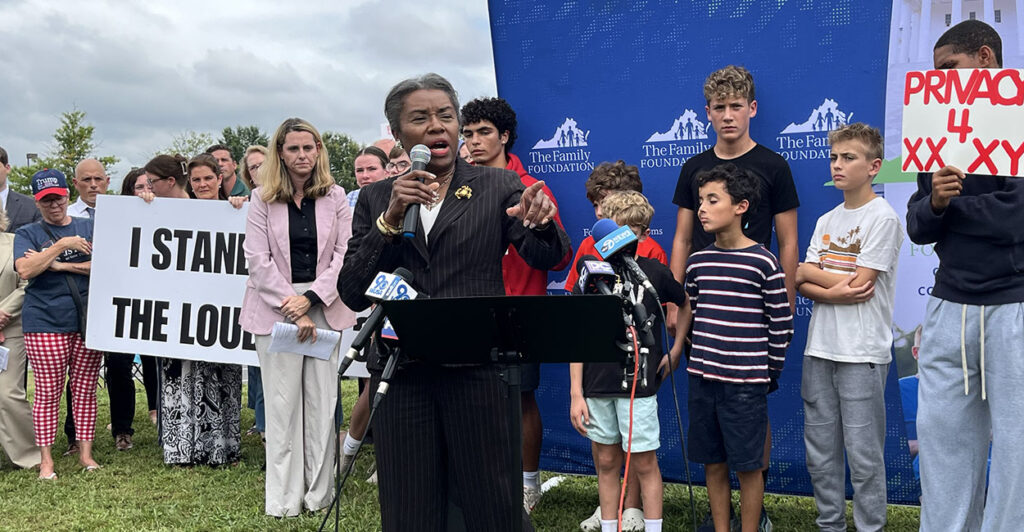 Winsome Earle-Sears in front of a sign reading "I Stand With The Loudoun 3"