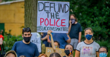 Protesters in masks hold up defund the police, Black lives matter banners