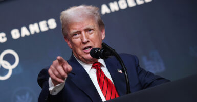 President Donald Trump points at someone, with a promotional signage for the 2028 Los Angeles Olympics behind him.
