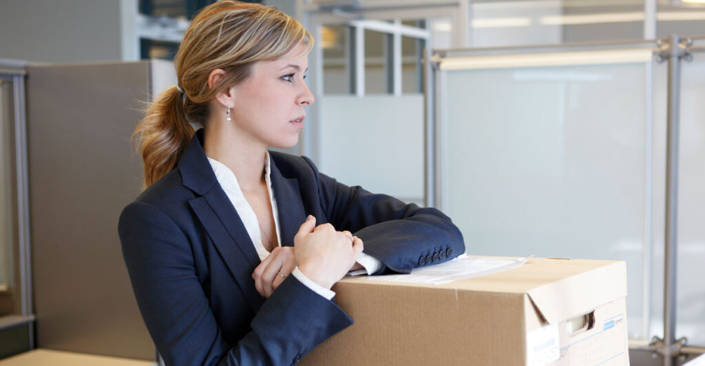 A young woman in a business suit packs up her office in in empty office suite