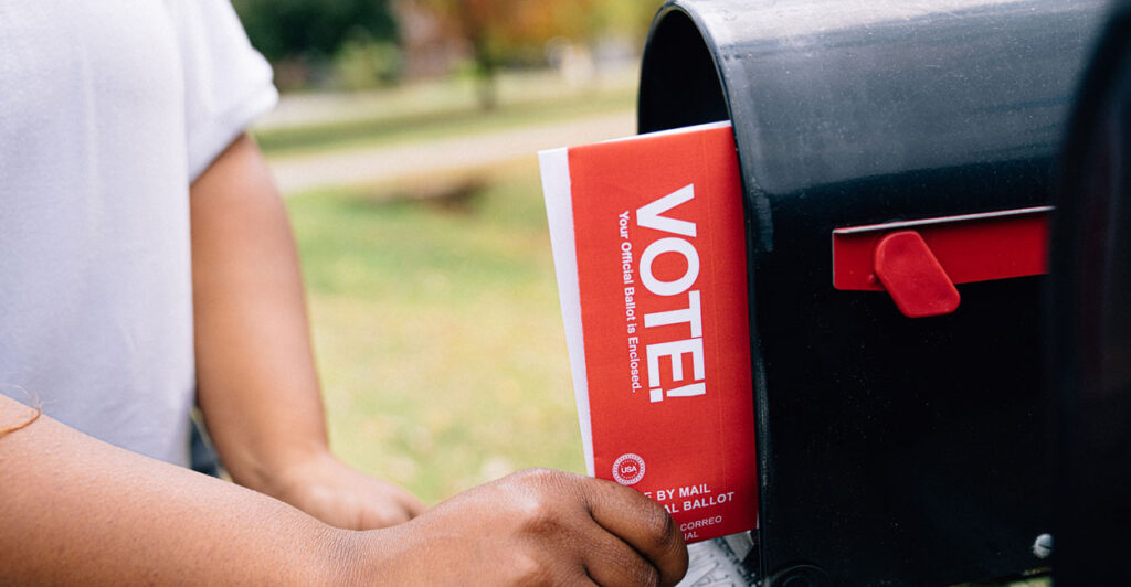 A person pulling a mail-in ballot from her roadside mailbox