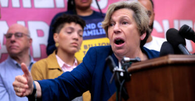 American Federation of Teachers President Randi Weingarten at a podium with multiple microphones speaking at a rally with rally goers behind her