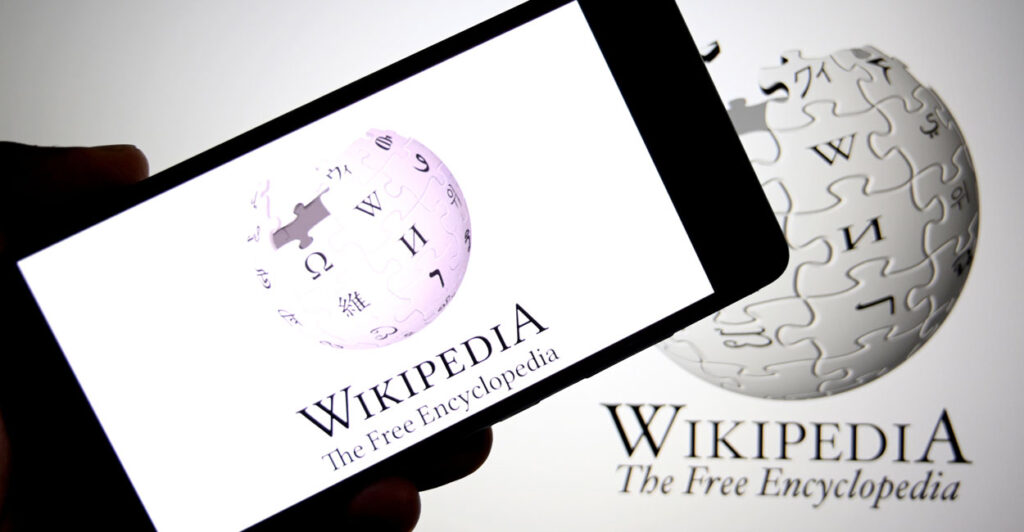 In a photo illustration, the Wikipedia logo is seen displayed on a smartphone and in the background.