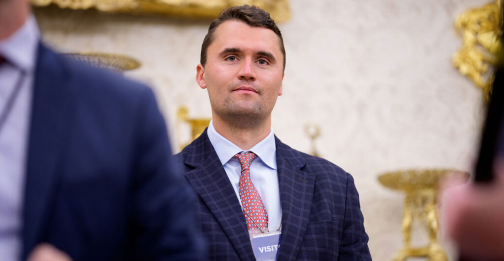 Charlie Kirk stands with his arms by his side as he looks straight forward.