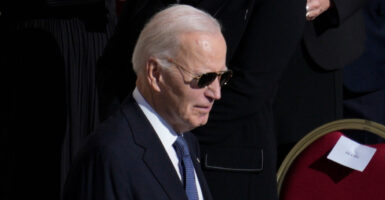 Joe Biden stands at a funeral while wearing his sun glasses.