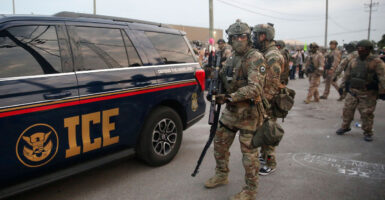 An Immigration and Customs Enforcement agent looks at a photograph while holding a gun next to an ICE SUV.