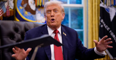 Donald Trump with his arms stretched sits at his desk in the Oval Office.