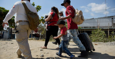 A family of migrants is seen walking outside in Mexico. One is holding a baby, and another holds the hand of a young boy and pulls a suitcase with his other hand.