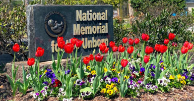 Gold-against-black sign for National Memorial for the Unborn, with red, purple and yellow flowers.