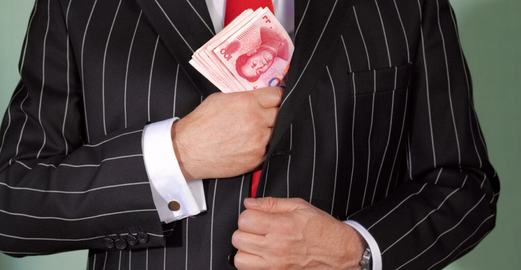 Torso of man in pinstripe suit putting a wade of Chinese money in his jacket.