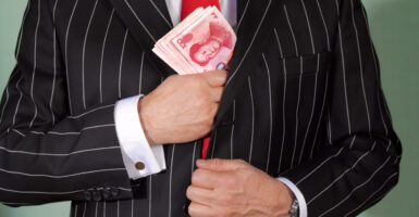 Torso of man in pinstripe suit putting a wade of Chinese money in his jacket.