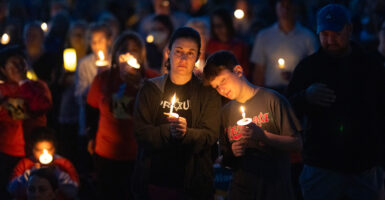 Boy puts head on shoulder of a woman at candlelight memorial for those shot at Annunciation School Church shooting.