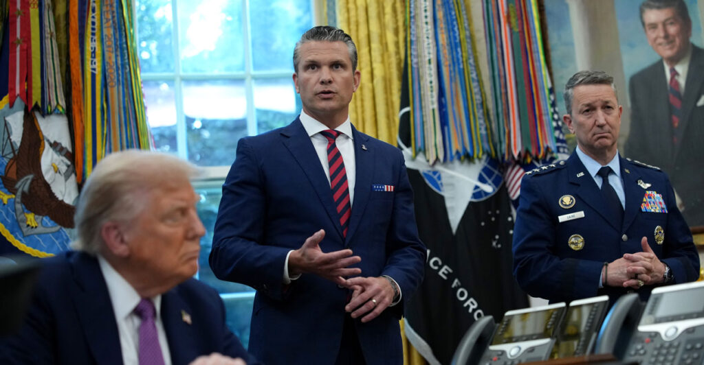 Pete Hegseth, standing, makes a point while in Oval Office, flanked by President Donald Trump and Chairman of the Joint Chiefs of Staff Air Force Gen. Dan Caine.