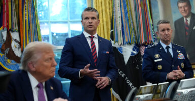 Pete Hegseth, standing, makes a point while in Oval Office, flanked by President Donald Trump and Chairman of the Joint Chiefs of Staff Air Force Gen. Dan Caine.