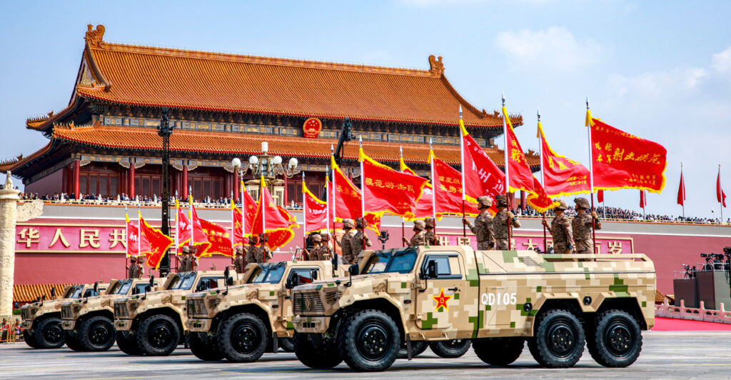 A line of Chinese-flag bearing military vehicles roll through Tiananmen Square.