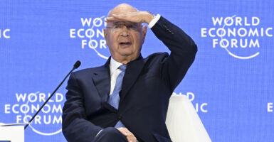 Klaus Schwab looks out over the audience at a World Economic Forum meeting, his left hand shading his eyes.