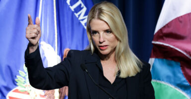 Pam Bondi, in a black suit, points during a press conference, with DOJ flag behind her.