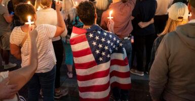 A young man wrapped in American flag is among a crowd gathered for a candlelight vigil honoring Charlie Kirk.