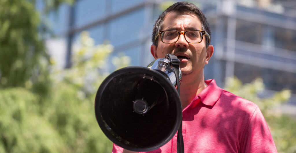 Jose Garza in a pink shirt speaks into a megaphone.