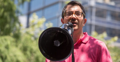 Jose Garza in a pink shirt speaks into a megaphone.