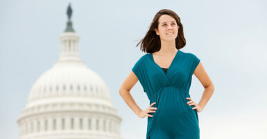 Young, confident woman in emerald outfit, with hands on hips, stands with U.S. Capitol dome behind her.