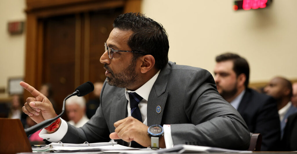 Kash Patel in a gray suit, leans forward to microphone while testifying in a House hearing.