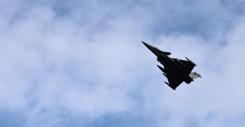 A French Rafale fighter get soars against a partly cloudy sky.