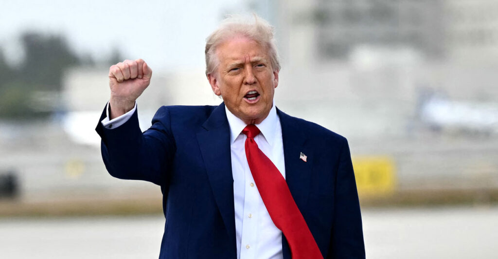 President Trump on a tarmac, fist raised, wind blowing his red tie.