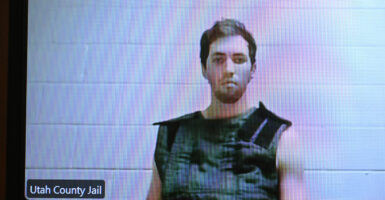 Tyler Robinson in a safety vest appears on screen against a white wall during a court appearance.