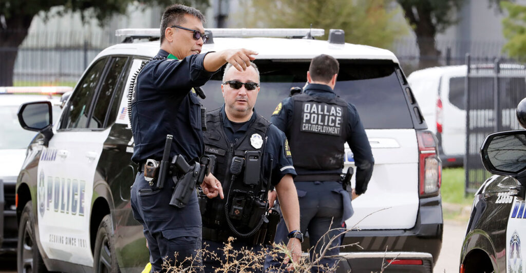 A Dallas police officer points out something to a fellow officer as another officer stands in front of a Dallas police vehicle.