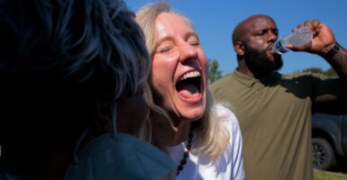 Virginia gubernatorial candidate Abigal Spanberger her mouth wide open in laughter at a campaign event. Behind her a black man swigs a bottle of water.