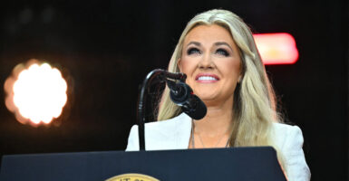 Erika Kirk, in a white outfit, smiles while standing behind a podium with the Presidential Seal.