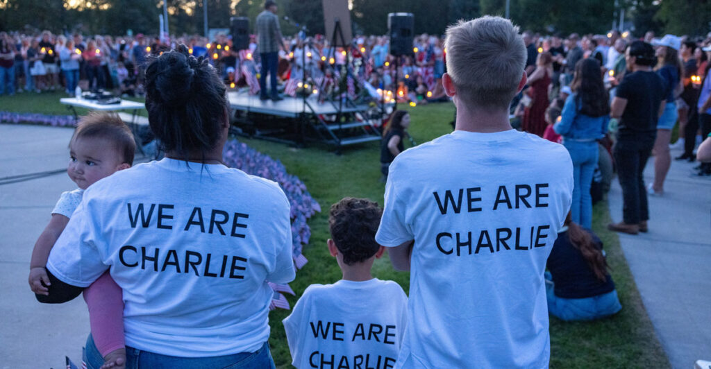 A mother holding a baby, father and son wear white shirts with black lettering reading "We Are Charlie" as they attend a vigil for Charlie Kirk.