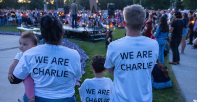 A mother holding a baby, father and son wear white shirts with black lettering reading "We Are Charlie" as they attend a vigil for Charlie Kirk.