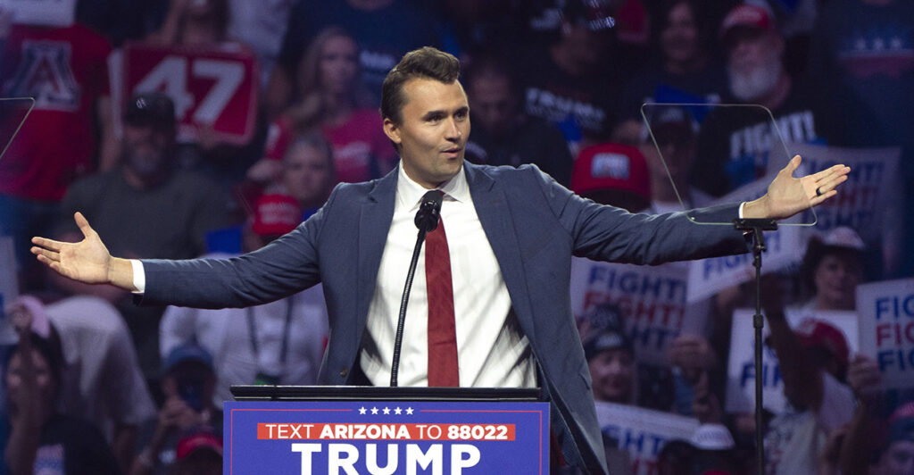 Charlie Kirk in a suit with his hands out