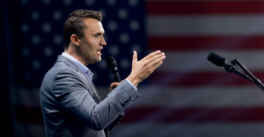 Profile view of Charlie Kirk in a suit in front of an American flag