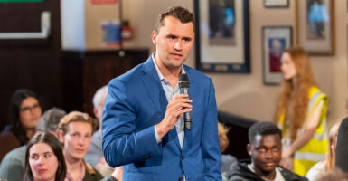 Charlie Kirk holds a microphone in front of students.