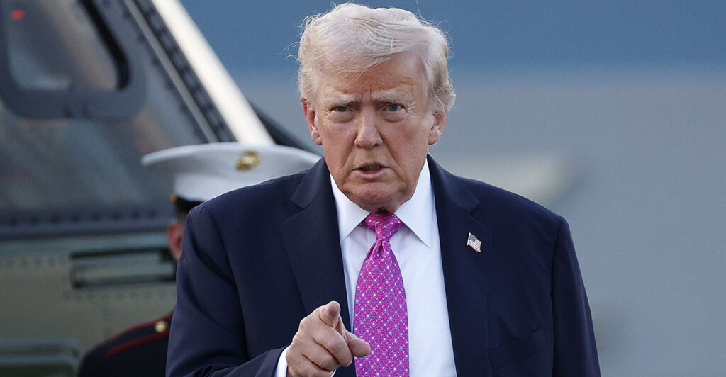 Donald Trump in a blue suit with a blue tie points.