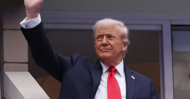 Donald Trump in a suit raises his hand