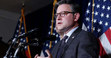 Mike Johnson looks out as he speaks into a bank of microphones, American flags behind him.