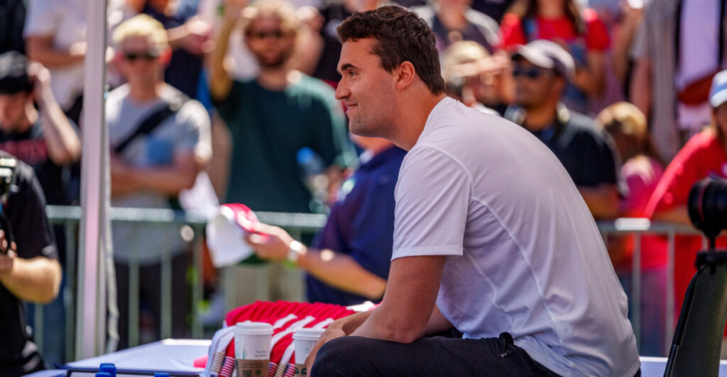 Charlie Kirk sits and smiles at an event.