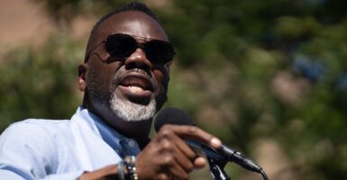 Brandon Johnson stands behind a podium and microphone and talks while pointing with his right hand.