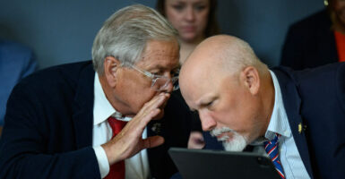 Ralph Norman of South Carolina whispers into the ear of Chip Roy of Texas in a Congressional hearing room.