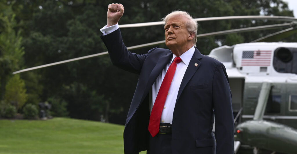 President Trump, in front of his Marine One helicopter, raises his fist.