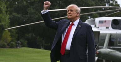 President Trump, in front of his Marine One helicopter, raises his fist.