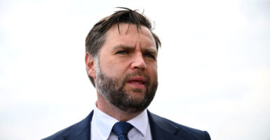 A close up photo shows JD Vance speaking, with a white sky behind him.