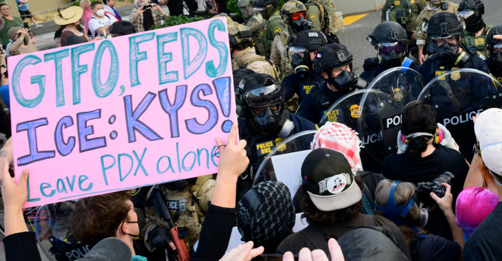 Federal agents confront protesters outside of the U.S. Immigration and Customs Enforcement building. One protest sign reads "GTFO, Feds. ICE: KYS! Leave PDX alone."