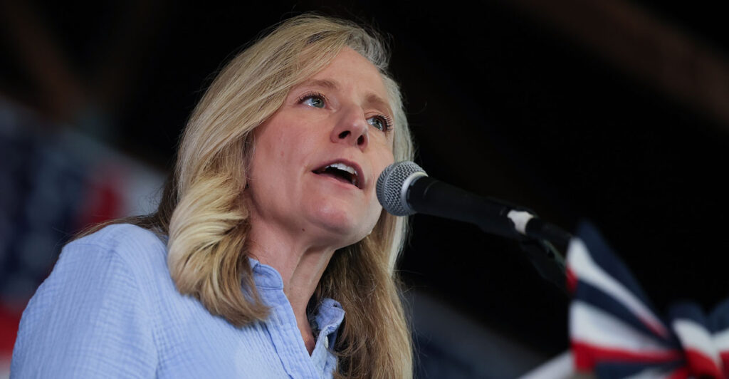 Abigail Spanberger in a blue button-down shirt speaks into a microphone at a rally